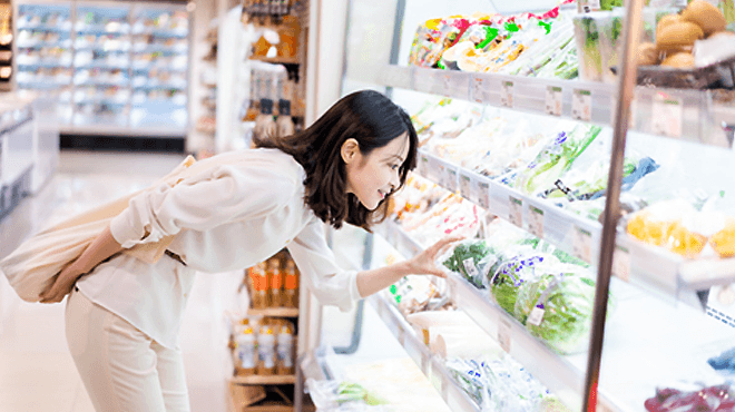 女性がスーパーで野菜を手にしようとしている画像