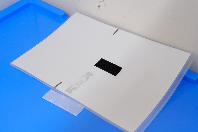 伝票はクリアフォルダに挟まれ、コンテナの山に乗せる専用蓋にマジックテープで固定のイメージ