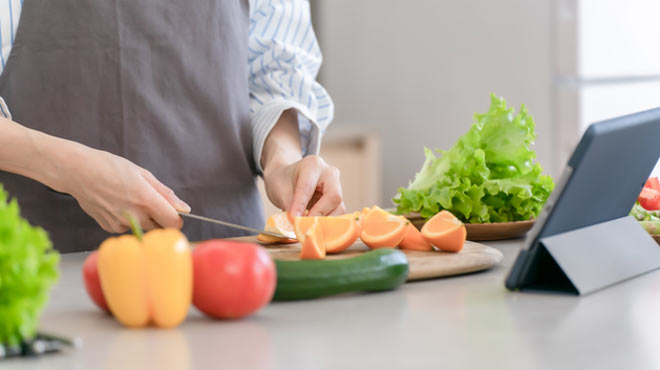 タブレットを見ながらくだものをカットしているイメージ画像