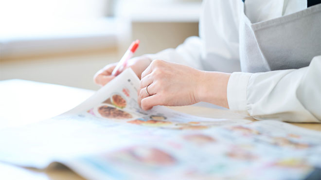 ペンを持ってチラシをめくる手元のイメージ画像