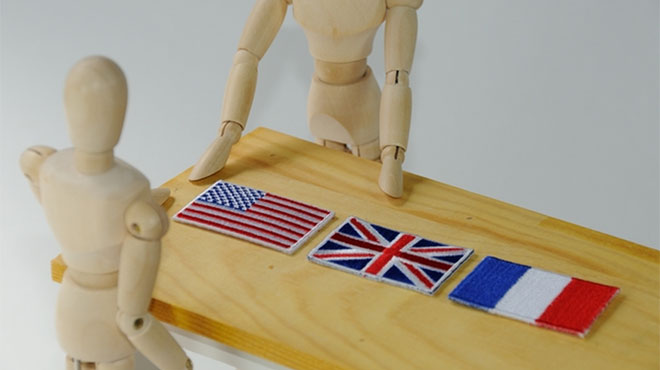 テーブルに置かれたアメリカ、イギリス、フランスの国旗と2体の人形のイメージ画像