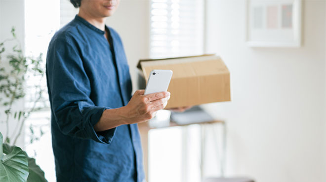 小包を持ってスマートフォンを見る人のイメージ画像