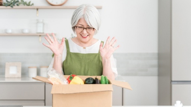 野菜が入った段ボールを開けて喜んでいる女性のイメージ画像