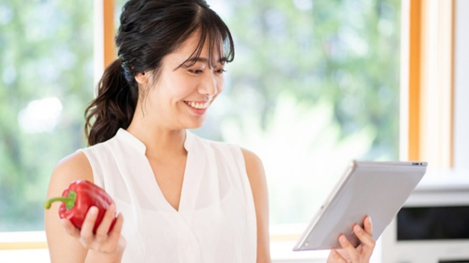 食材を片手にタブレットを確認している女性のイメージ画像