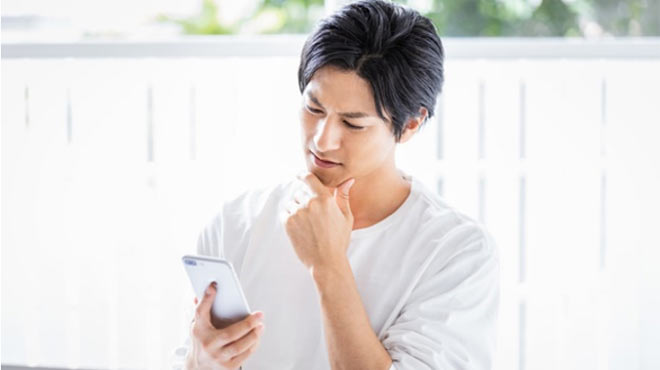 スマートフォンを見て悩む男性