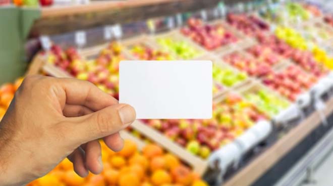 スーパーマーケットの果物売り場にて手にカードを持っているイメージ画像