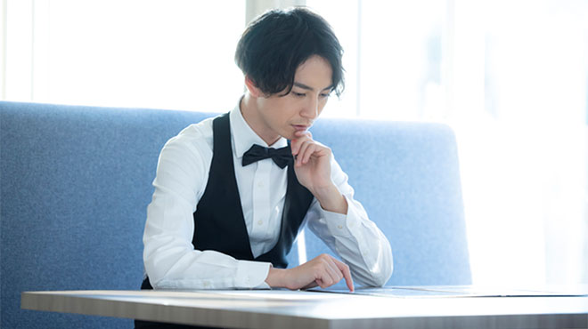 テーブルに肘をついて思案する男性のイメージ画像