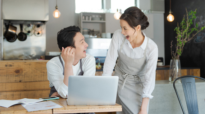飲食店経営者らしき人たちがパソコンを前に顔を見合わせるイメージ画像