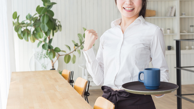 カップを載せたトレイを持って笑顔を見せる女性のイメージ画像