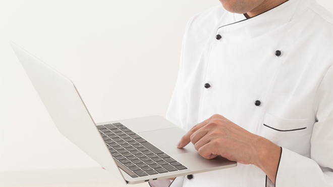 ノートパソコンを操作するコックコートを着た人のイメージ画像