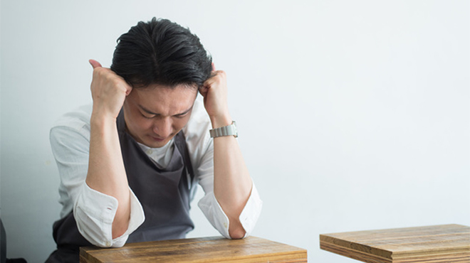 頭を抱える飲食店経営者らしい男性のイメージ画像
