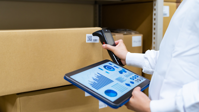 倉庫内でハンディ端末を用いて箱に貼付されたQRコードを読み取る業務シーン