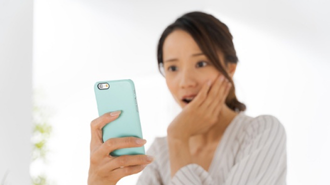 スマートフォンの画面を見て驚く女性のイメージ画像